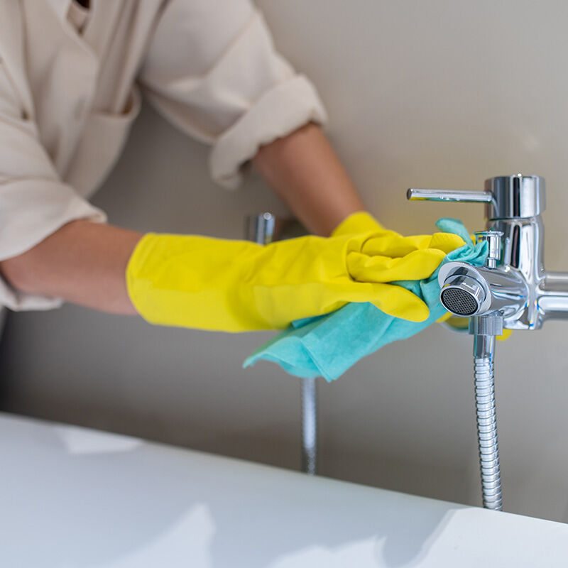 badewannenarmatur wird geputzt mit gummihandschuhen und gr&uuml;nem lappen