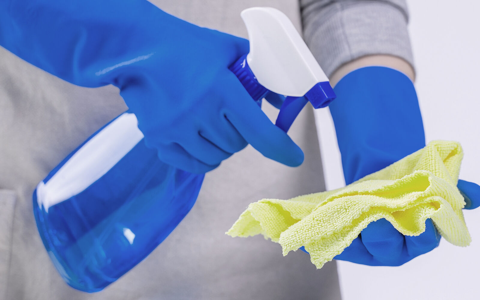 Person mit Spr&uuml;hflasche und Reinigungstuch in der Hand